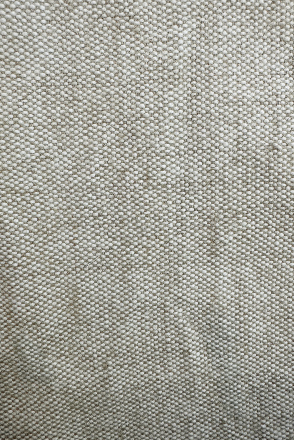 A close-up view of woven warm beige fabric reveals the intricate texture of Tierra’s Jute & Organic Cotton Blend Headboard Cushion Cover. The organic fibers, visible in the natural weave pattern, emphasize the material’s grounding feel, durability, and breathable comfort designed for a clean, calming sleep environment.