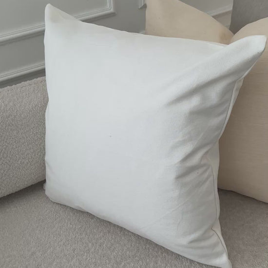 A video of the sofa with a crisp white pillow placed in front of beige and navy cushions, underscoring the refined simplicity, durability, and toxin‑free comfort of Tierra’s 100% organic cotton accent pillow cover. Together, the images reflect elevated home comfort, expert craftsmanship, and the effortless beauty of natural materials.