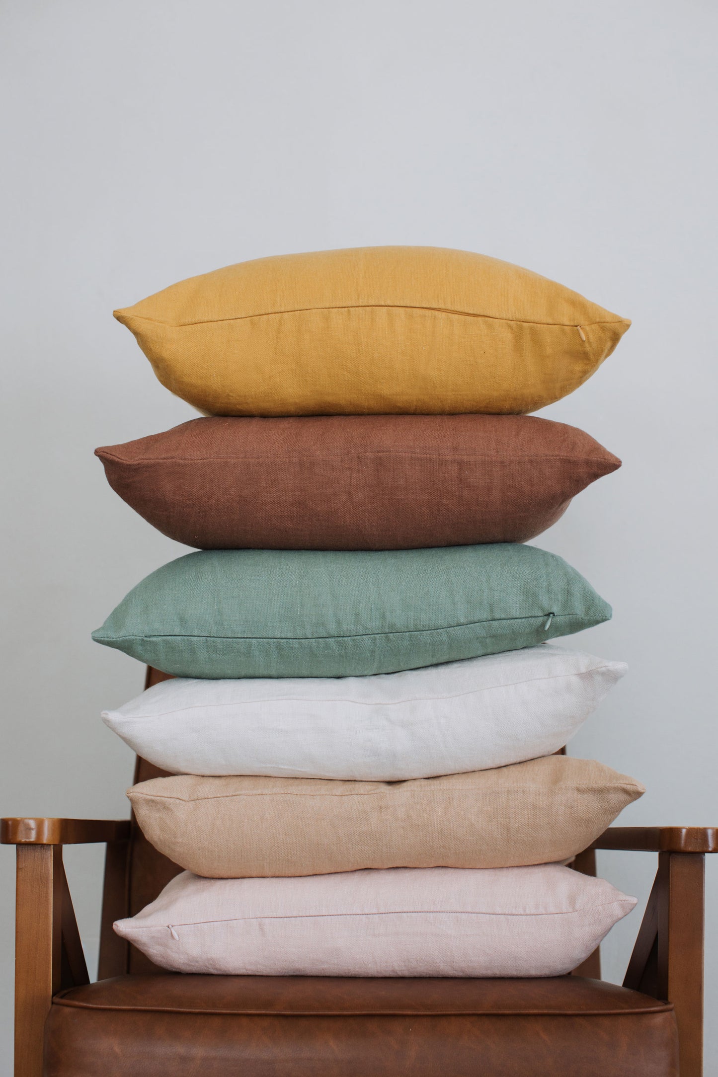 Tower of Tierra's 100% linen accent pillows in every available color displayed on a leather chair to showcase the full linen color collection.