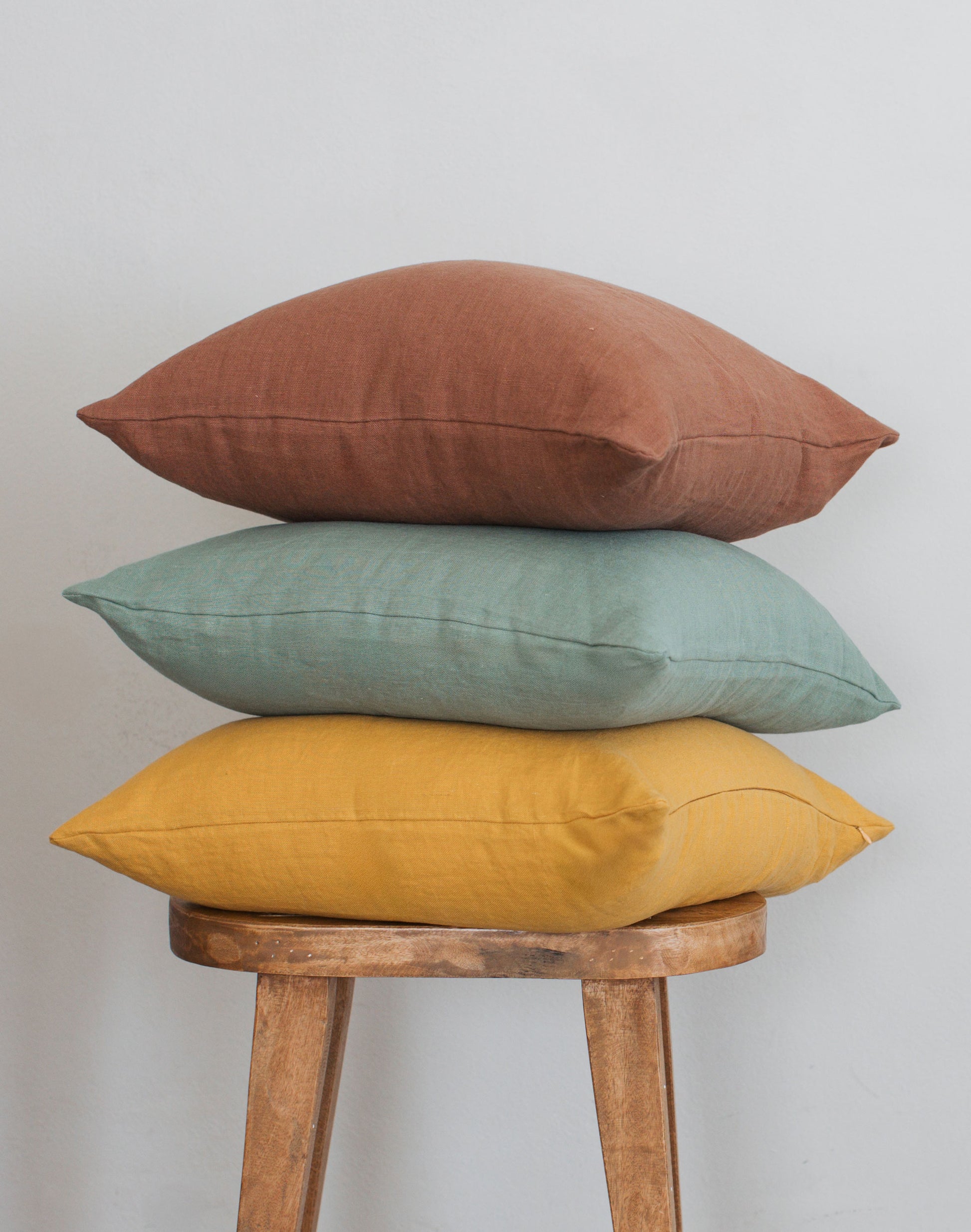 Three bright-colored Tierra 100% linen accent pillows stacked on a stool against a white wall showcasing the vibrant linen color collection.