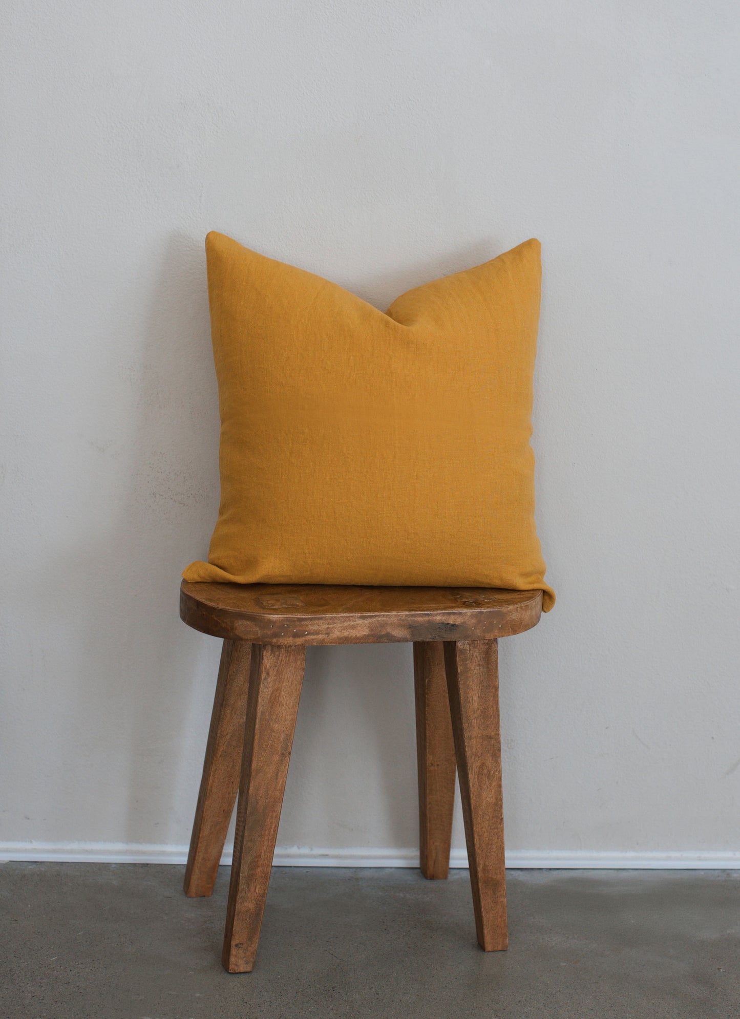 Tierra 100% linen accent pillow in yellow displayed on a wooden stool against a white wall with a clean modern aesthetic.