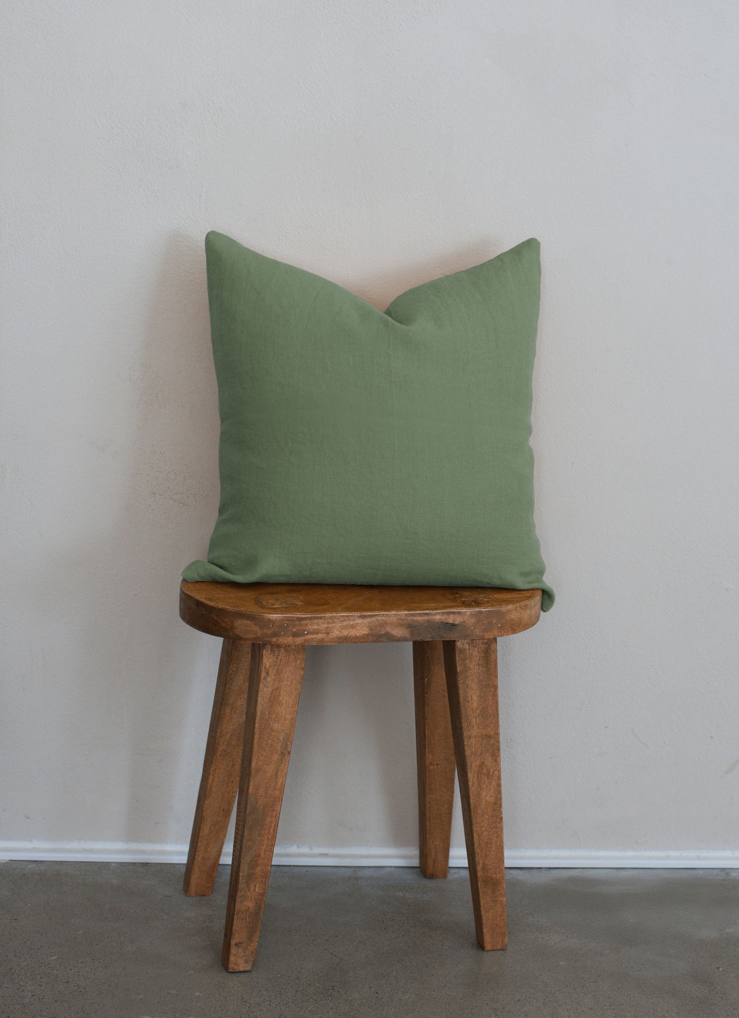Tierra 100% linen accent pillow in green displayed on a wooden stool against a white wall with a clean modern aesthetic.