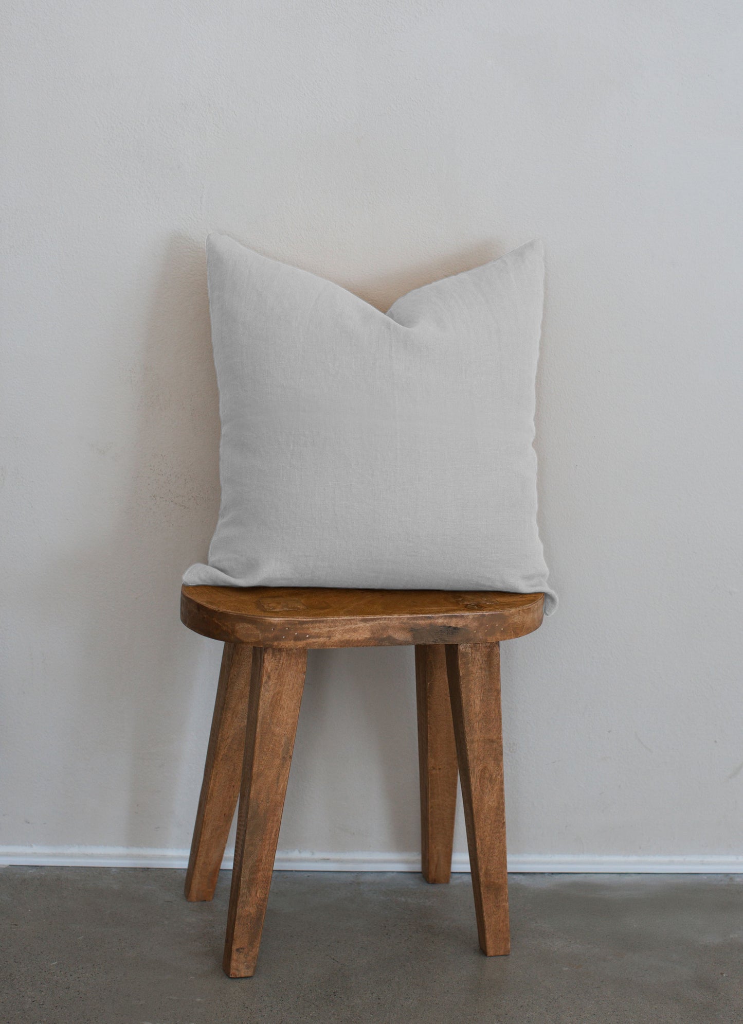 Tierra 100% linen accent pillow in white displayed on a wooden stool against a white wall with a clean modern aesthetic.