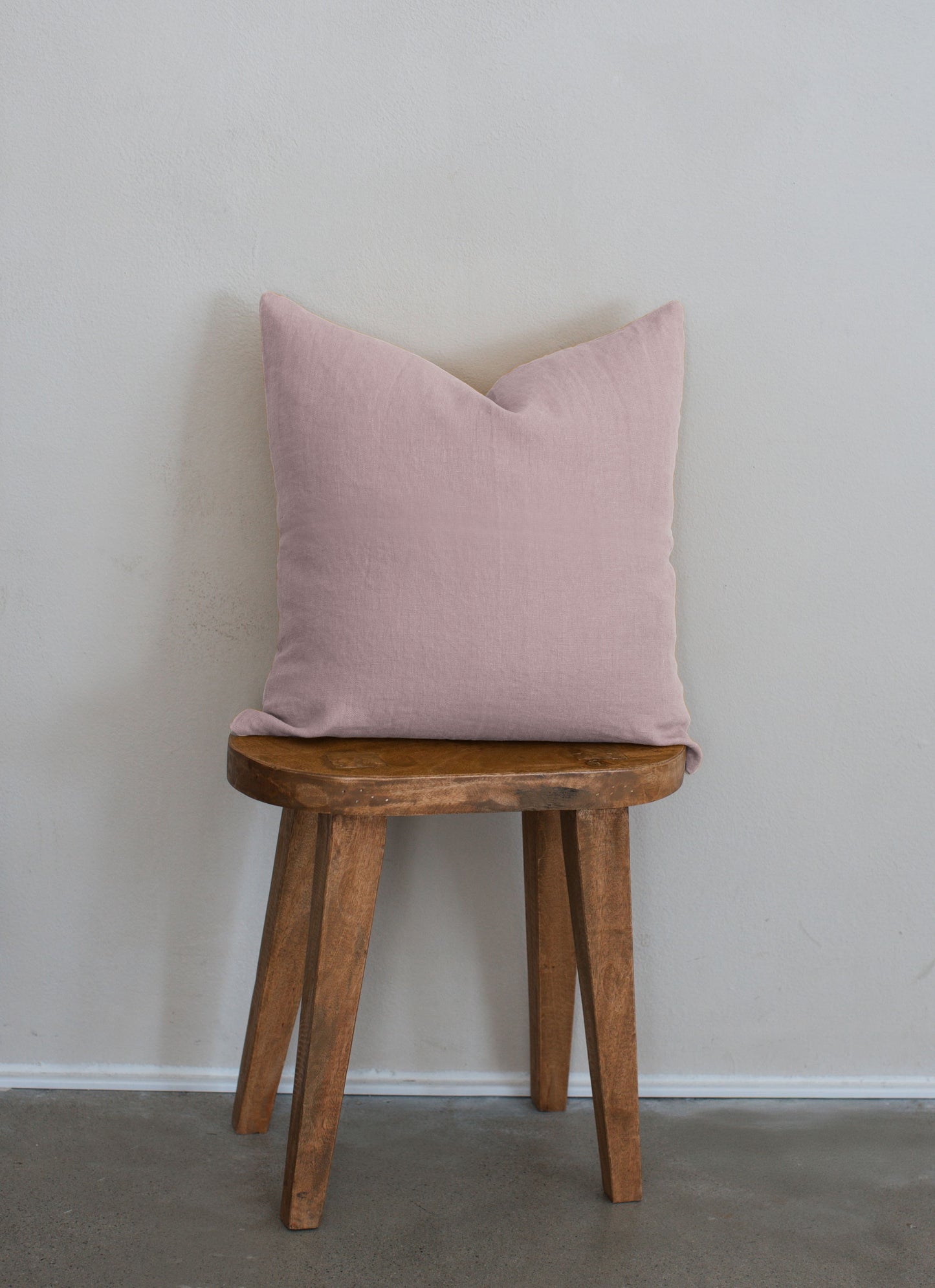 Tierra 100% linen accent pillow in pink displayed on a wooden stool against a white wall with a clean modern aesthetic.
