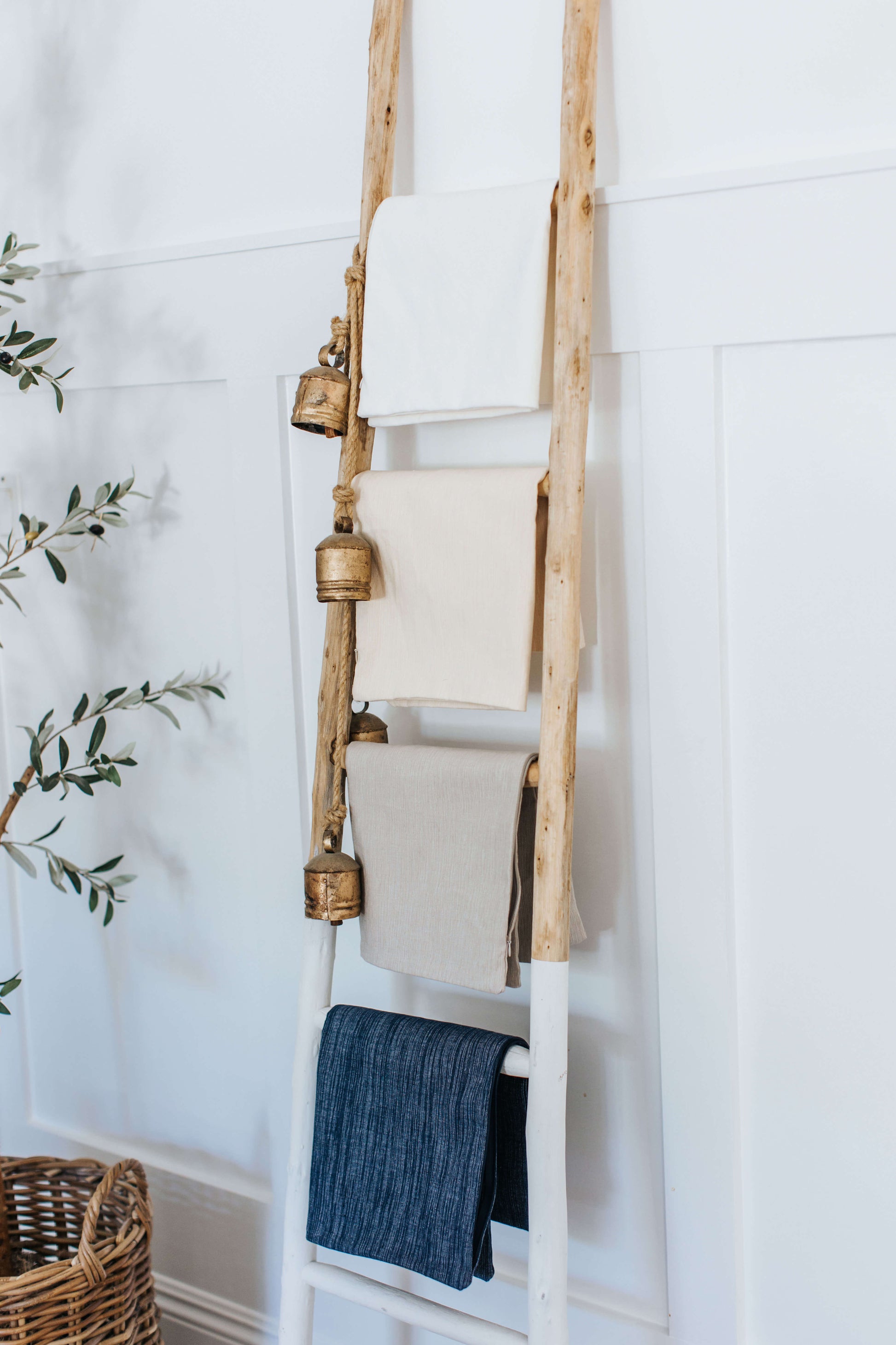 The image shows a wooden ladder used as a decorative rack for folded accent pillow covers in natural and navy tones, reinforcing the clean, understated aesthetic the pillow covers complements.