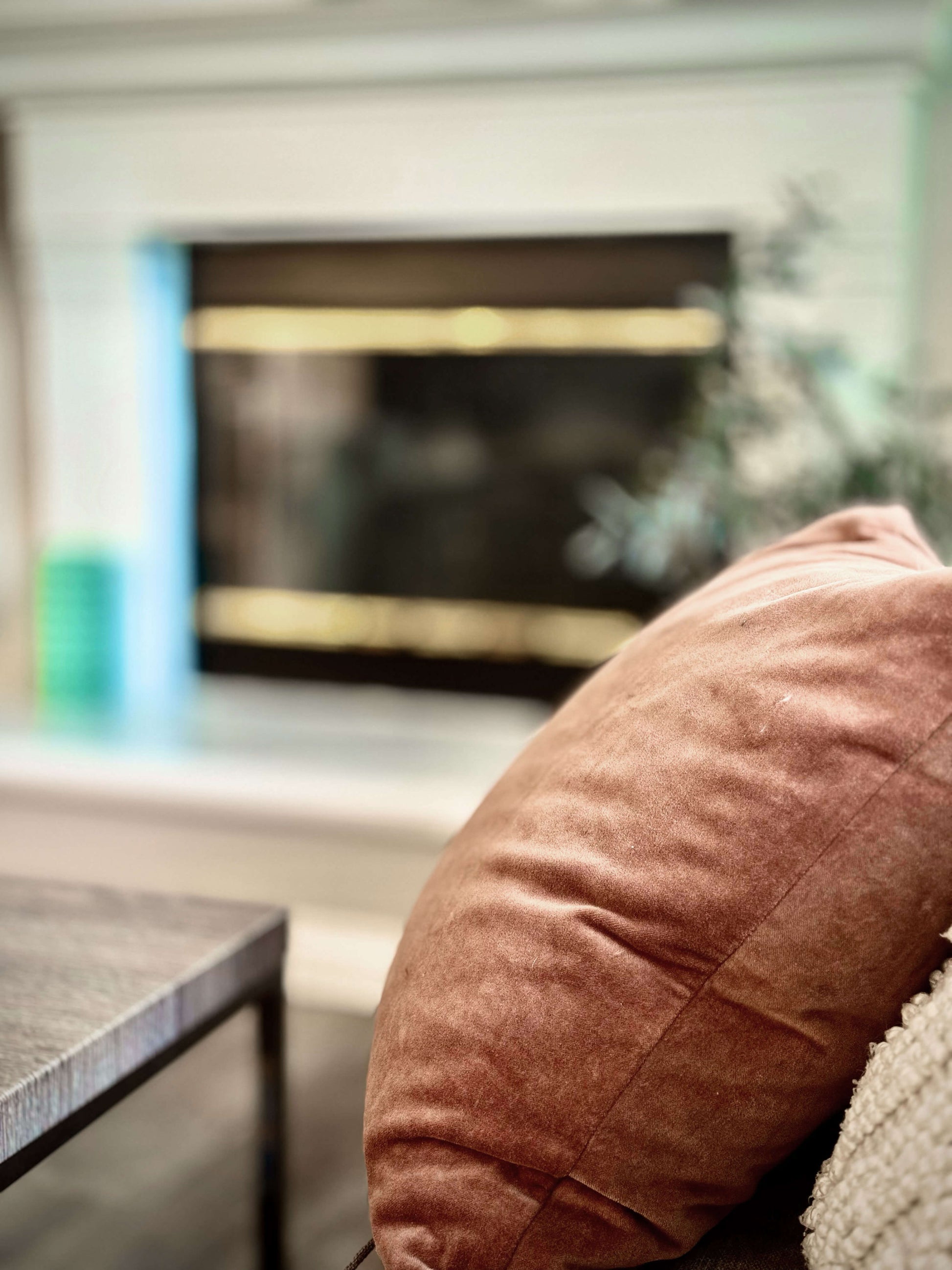The scene panel presents a chestnut‑colored accent pillow on a sofa with a blurred fireplace and greenery in the background, creating a serene, comforting atmosphere. 