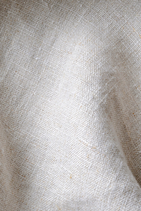 The image offers a close up of textured beige linen fabric, revealing its airy weave and naturally relaxed drape. 