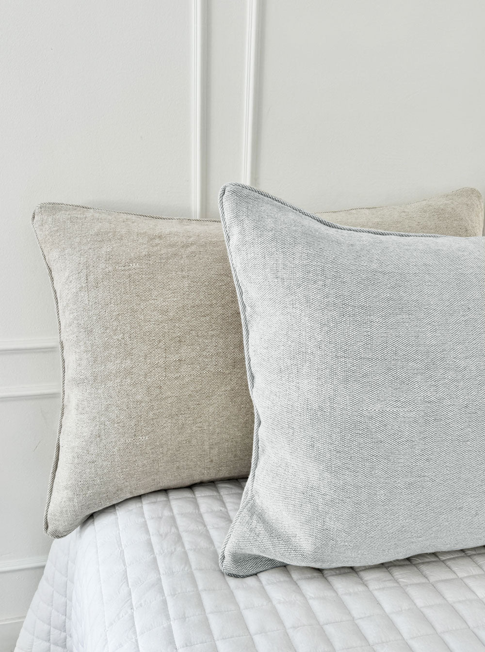 A serene bedroom setup shows the difference in hues with the light gray and the warm beige headboard cushion. Paired with soft neutral bedding and gentle natural light, the cushion cover reflects the blend’s breathable softness and refined, toxin‑free craftsmanship.