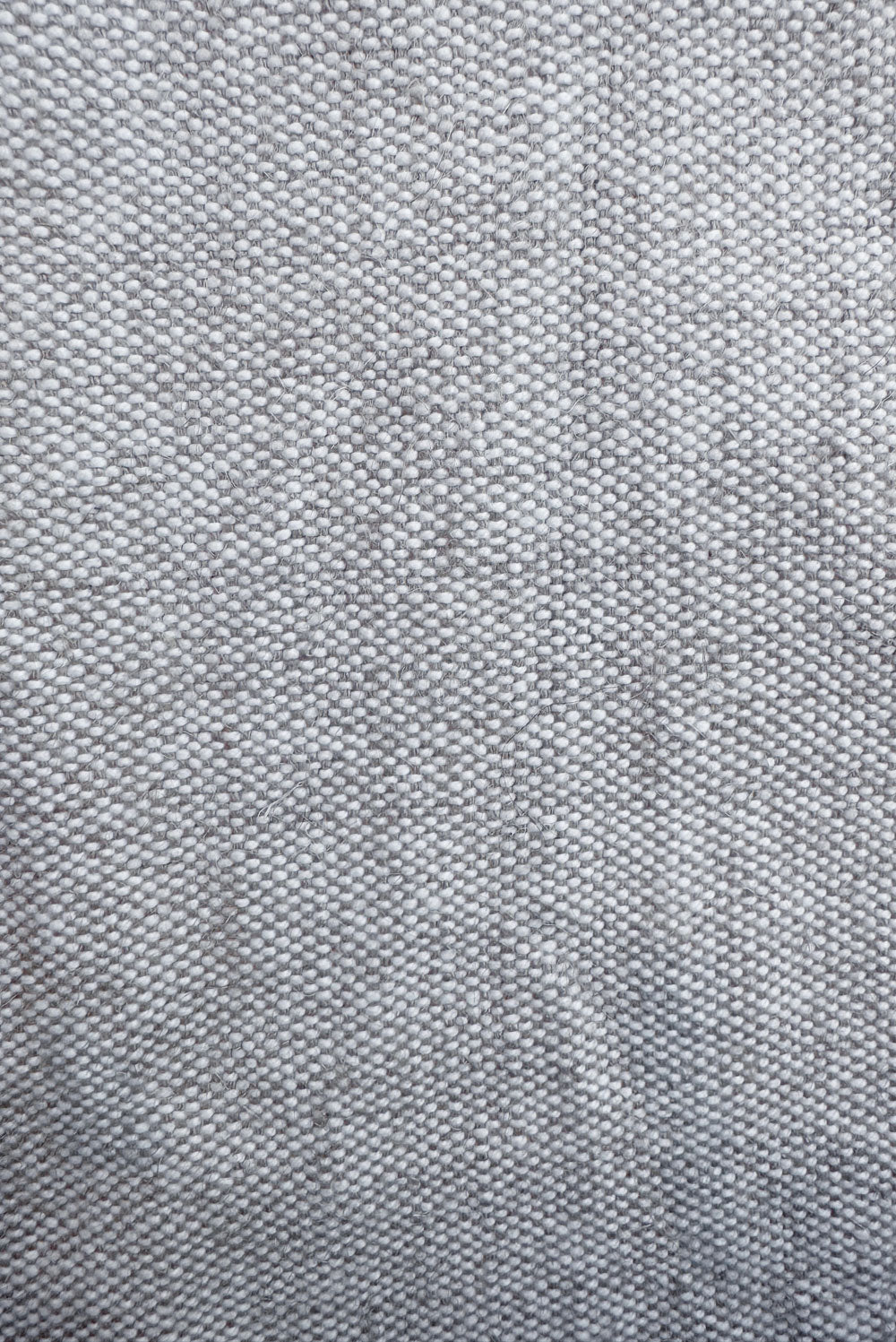 A close-up view of woven light gray fabric reveals the intricate texture of Tierra’s Jute & Organic Cotton Blend Headboard Cushion Cover. The organic fibers, visible in the natural weave pattern, emphasize the material’s grounding feel, durability, and breathable comfort designed for a clean, calming sleep environment.