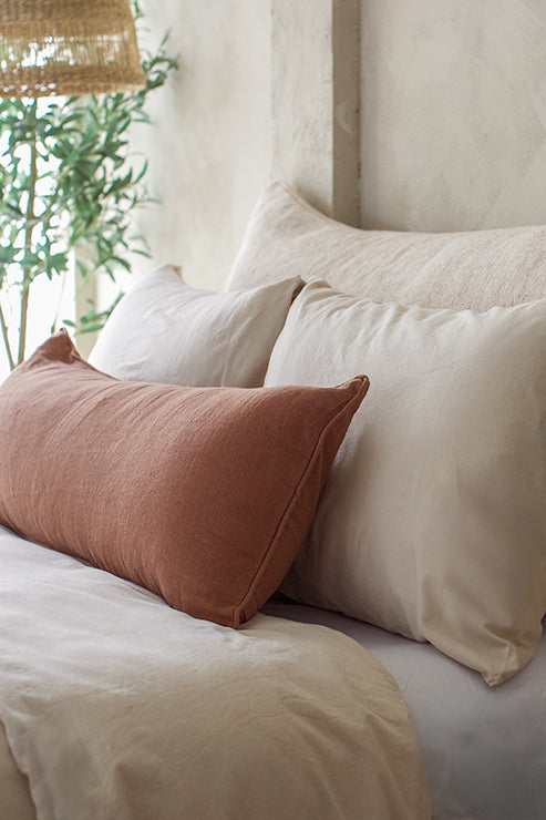 Tierra's 100% linen lumbar pillow in a chestnut color paired with a beige jute blend Headboard Cushion in warm earthy tones in an organic modern setting.