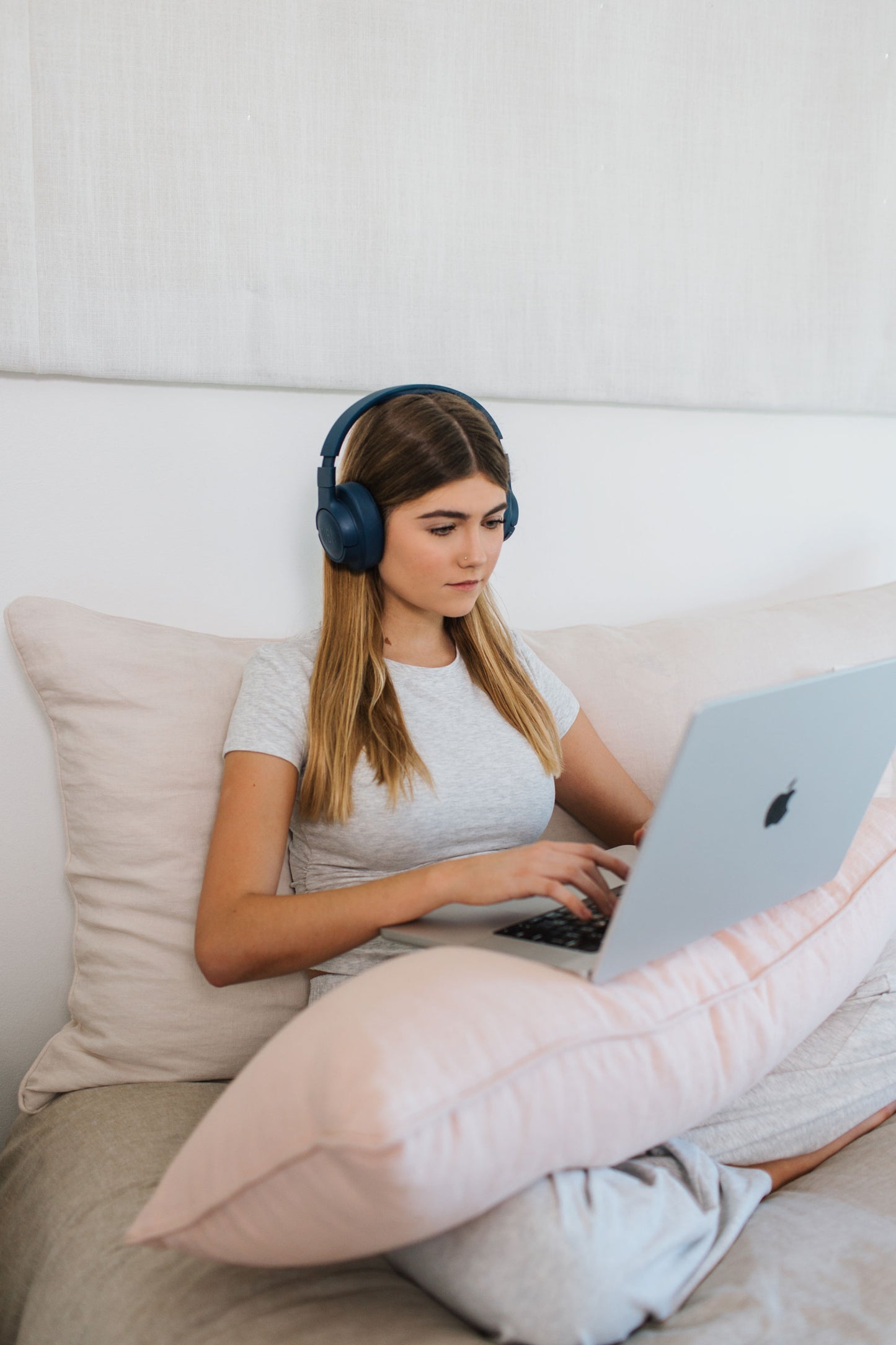 Teenage girl relaxing in bed with laptop, leaning against a white velvet washable Headboard Cushion and using a pink velvet lumbar pillow for ergonomic support and comfort.